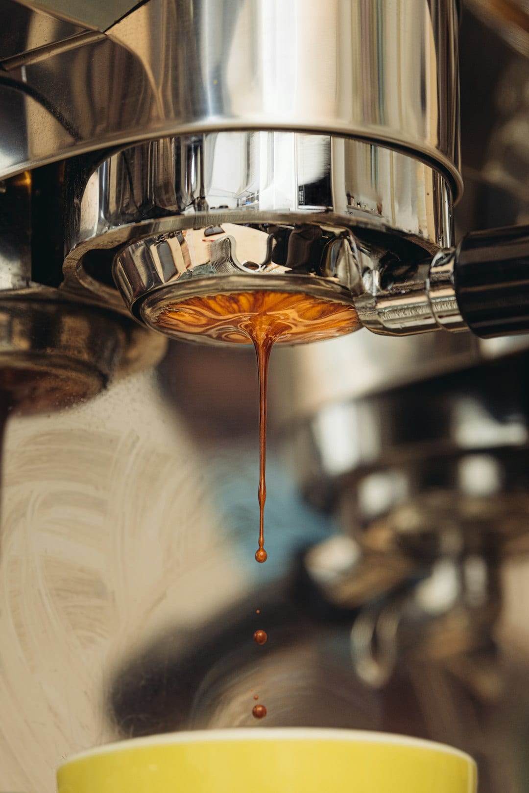 Espresso dripping from a bottomless portafilter into a yellow cup, with a thick layer of golden crema forming under the group head.