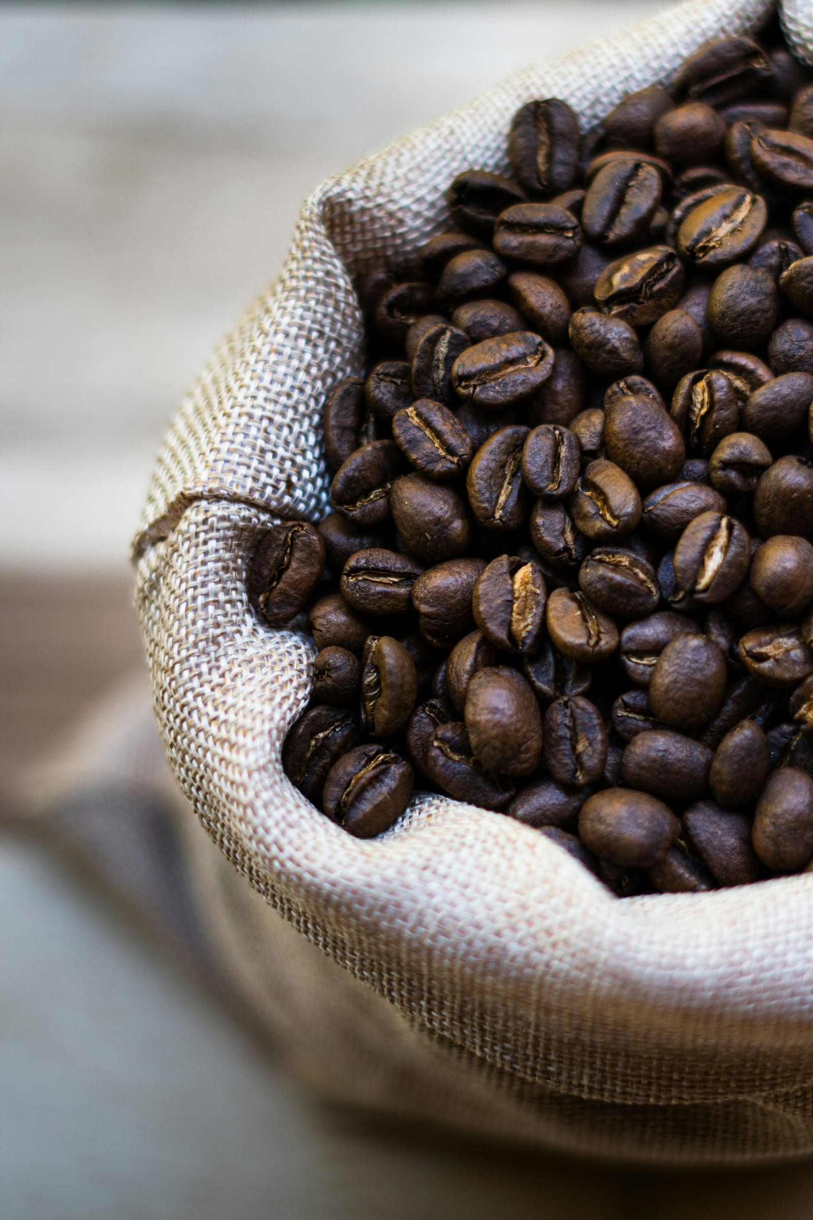 A burlap sack open to reveal a full pile of dark roasted coffee beans, photographed in close-up showing the beans' surface texture and characteristic center crease.