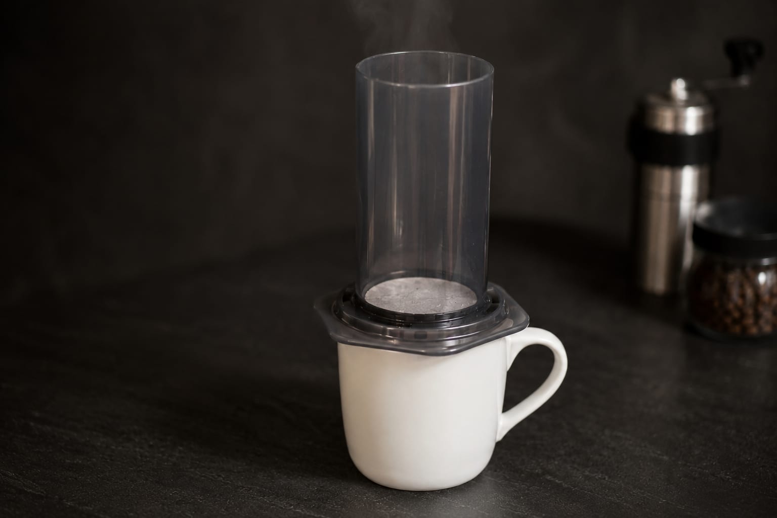 An assembled AeroPress resting on a white mug, its rinsed paper filter steaming, ready for coffee