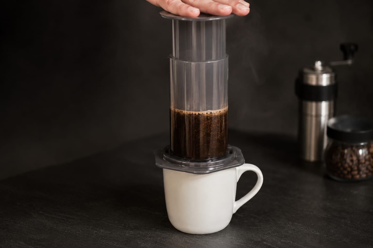 A hand pressing the AeroPress plunger down into the chamber on a white mug