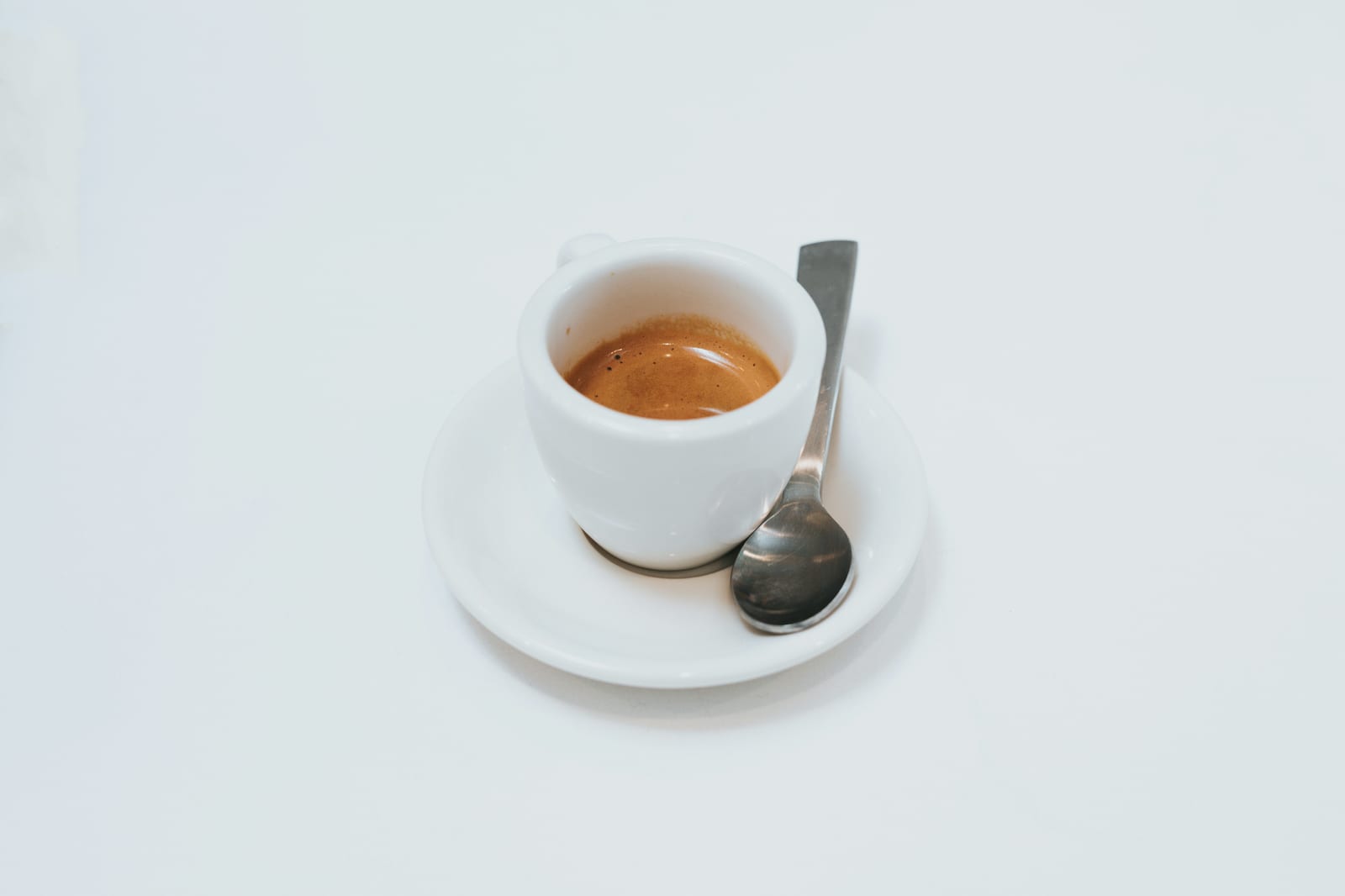 Una taza de espresso sobre un platito blanco con una cuchara de demitasse, recién extraído con crema dorada de café molido muy fino