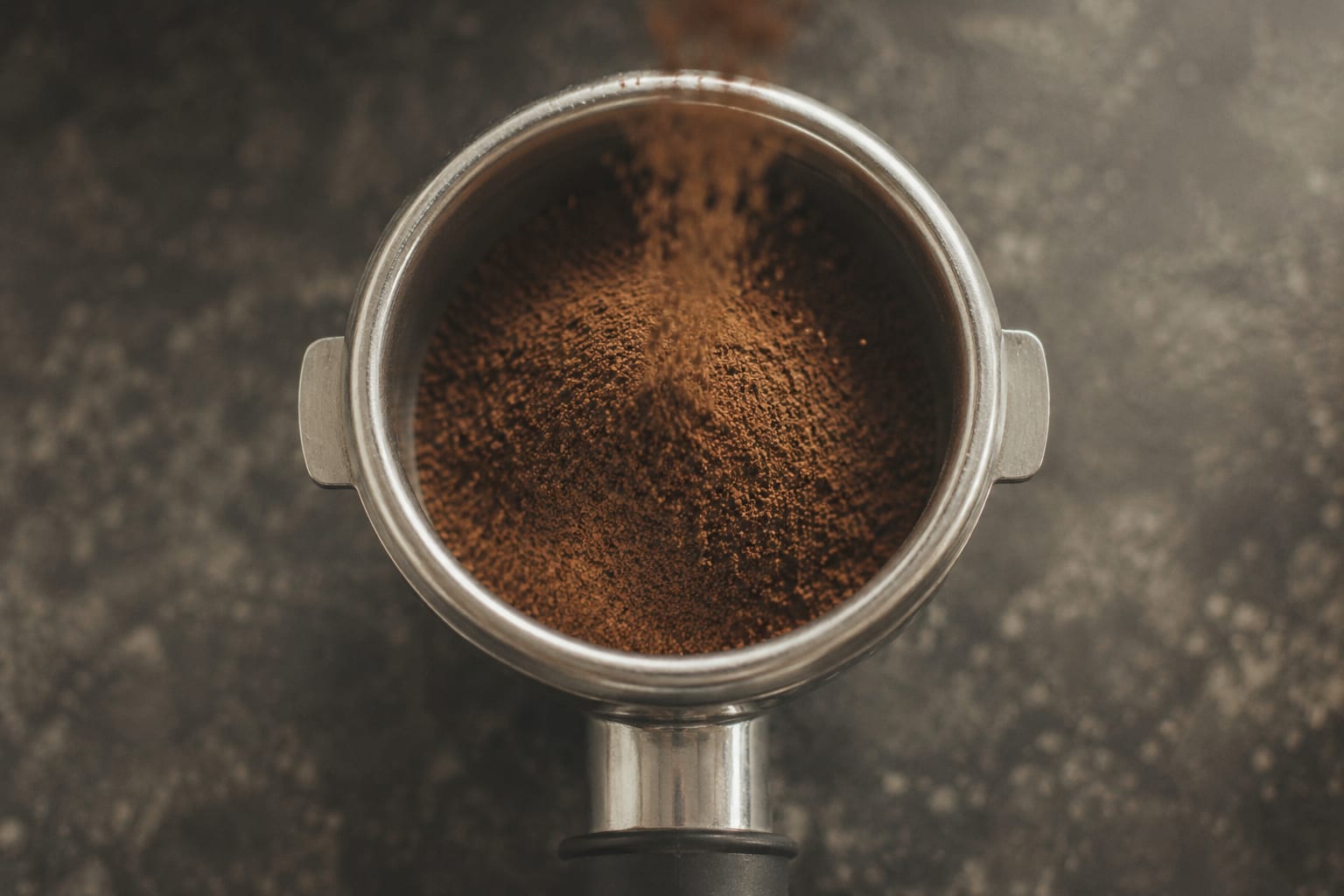 Vista cenital de una dosis de 18 gramos de café molido fino cayendo en una cesta de portafiltro de acero