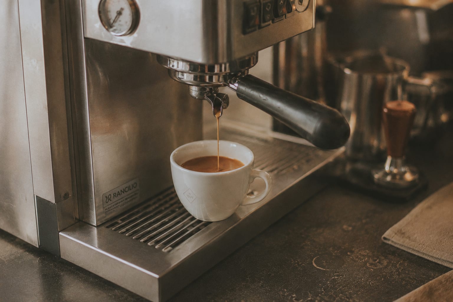 Espresso cayendo del portafiltro a una pequeña taza de cerámica blanca, con crema dorada formándose en la superficie